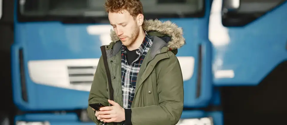 Verhuurder kijkt op zijn telefoon voor een vrachtwagen in de werkplaats